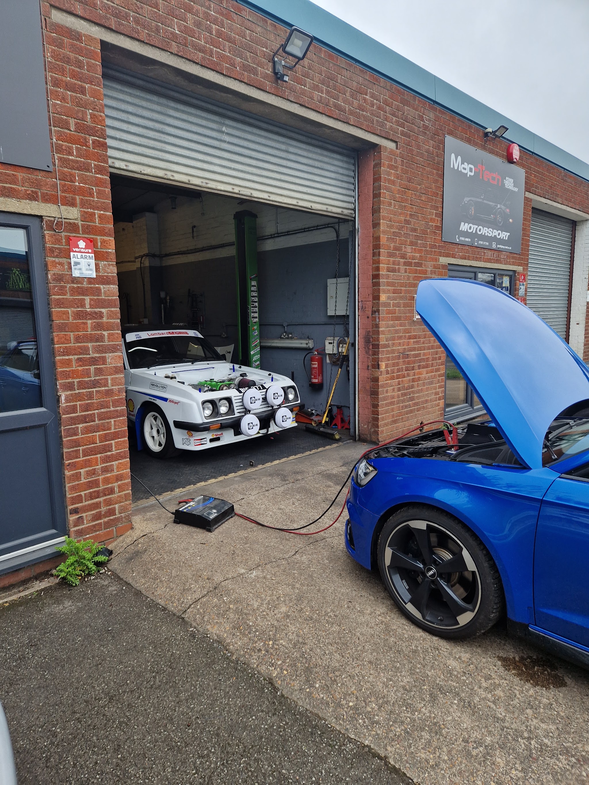 The Map-Tech unit with the roller door open, a white rally car inside and a blue car being worked on outside