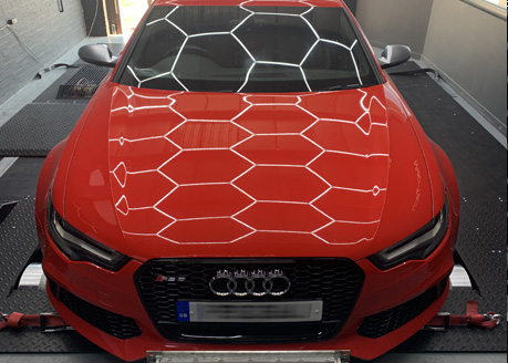 A red Audi RS on the dyno, hexagon lights reflected across the bonnet